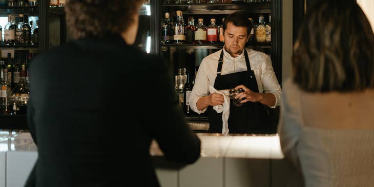 The barback is wiping the glassware after ensuring the the bar is well stocked.