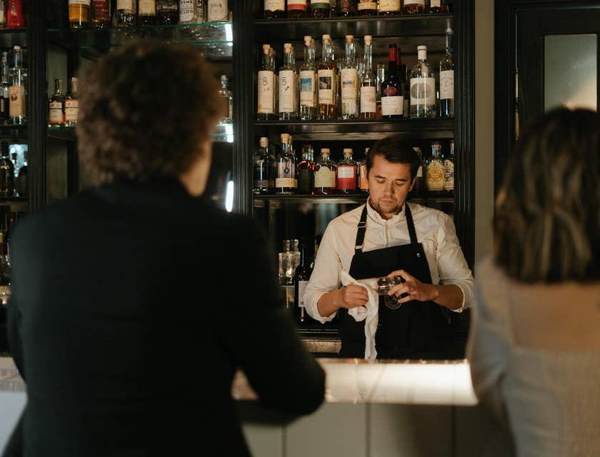 The barback is wiping the glassware after ensuring the the bar is well stocked.