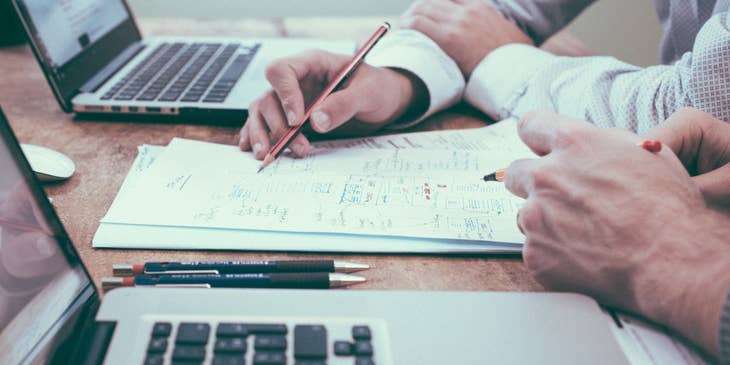 Dos personas de servicios financieros trabajando en sus portátiles y escribiendo en un papel.
