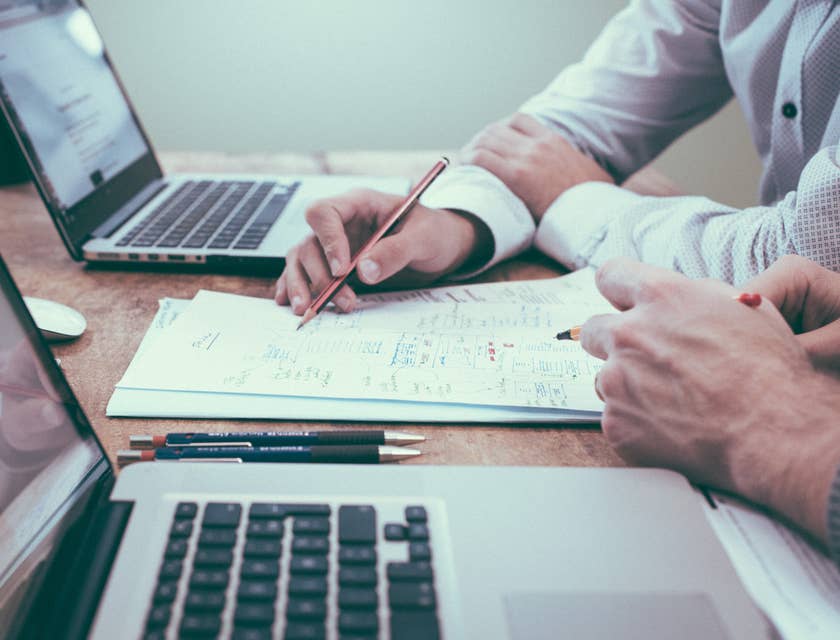 Dos personas de servicios financieros trabajando en sus portátiles y escribiendo en un papel.