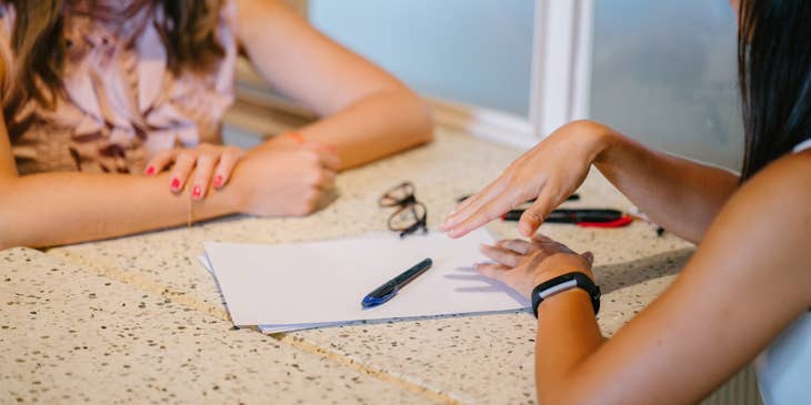 A Female Benefits Administrator in an office setting talking to an employee.