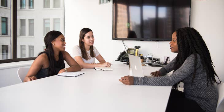 A Benefits Coordinator on her laptop in an office setting talking to employees.