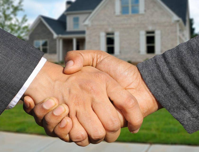 Un agente contratado por una bolsa de trabajo de bienes raíces dándole la mano a un cliente frente a una casa.