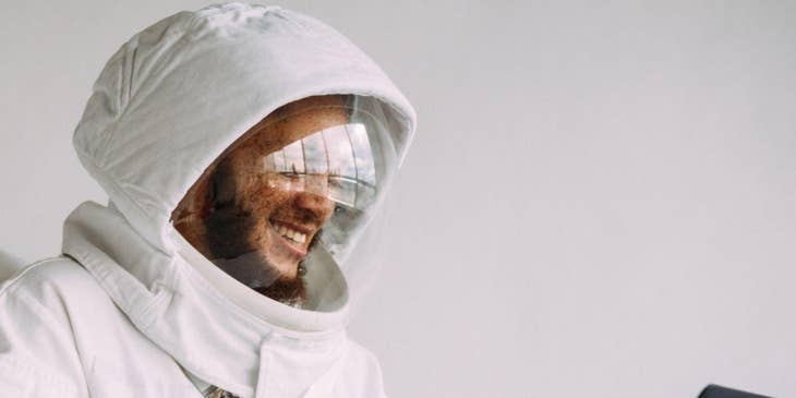 Un hombre con traje de astronauta contratado en una bolsa de trabajo para la industria aeroespacial trabajando en una laptop.