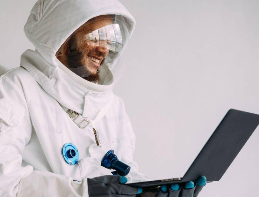 Un hombre con traje de astronauta contratado en una bolsa de trabajo para la industria aeroespacial trabajando en una laptop.