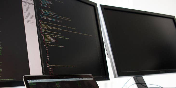 Un programador que trabaja en una computadora portátil y dos pantallas de computadora para una bolsa de trabajo para programadores.