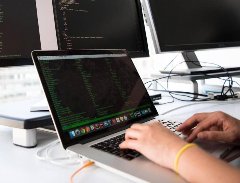 Un programador que trabaja en una computadora portátil y dos pantallas de computadora para una bolsa de trabajo para programadores.