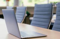 Sillas vacías en un escritorio con una computadora portátil abierta.