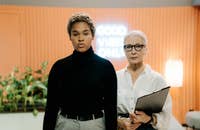 Una jefa parada detrás de su empleada mientras sujeta su CV.