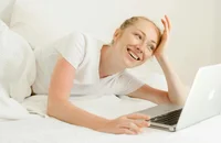 Una mujer usando una laptop acostada en su cama en un día económico.