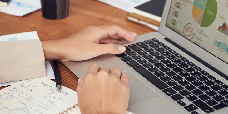 Compliance Analyst working on his laptop while his colleague taking down notes
