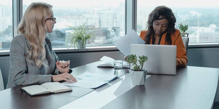 Development coordinator checking files while listening to colleague planning an event