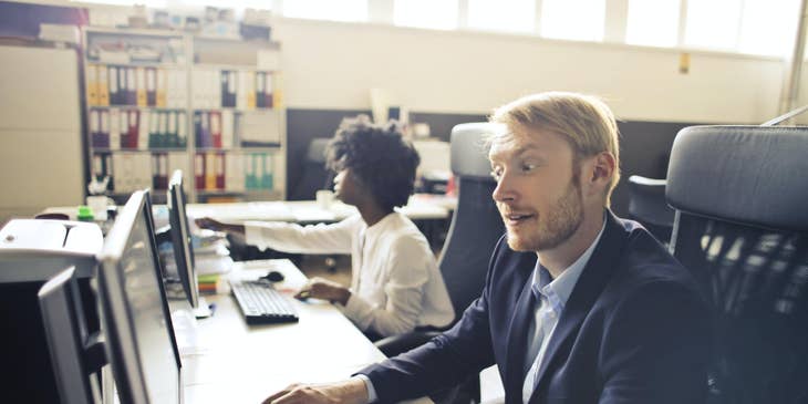 A Duty Manager on a computer working beside his employee.