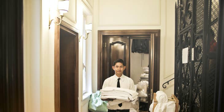 A Housekeeping Supervisor holding folded towels in the hallway of a hotel laundry area.