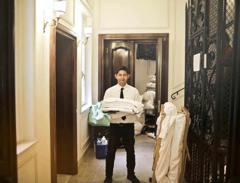 A Housekeeping Supervisor holding folded towels in the hallway of a hotel laundry area.