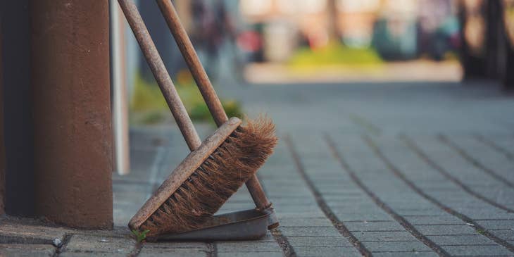 A janitor's broom and dustpan leaning against an exterior wall