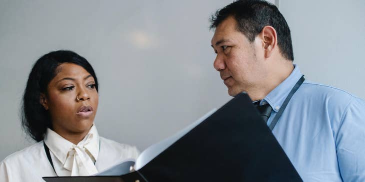 Office coordinator holding a document and talking to an office staff.