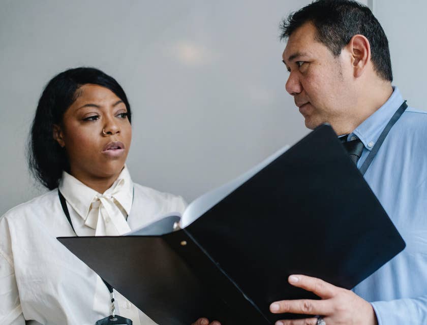 Office coordinator holding a document and talking to an office staff.