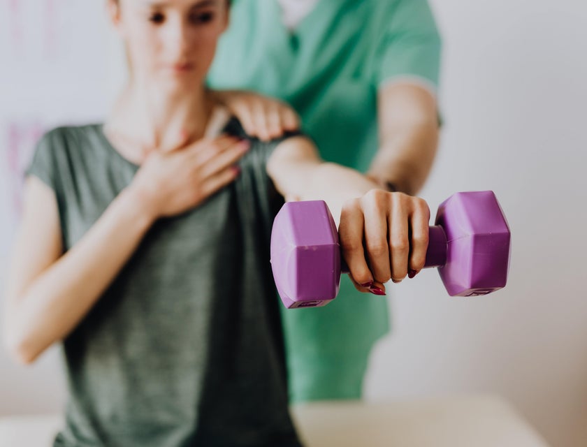 Physical therapy technician assists a patient in a light exercise using a dumbbell