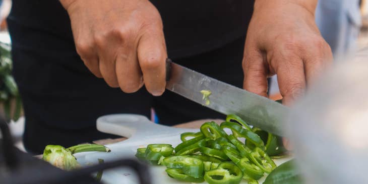 A prep cook in a kitchen holding a knife and slicing vegetables as preparation.