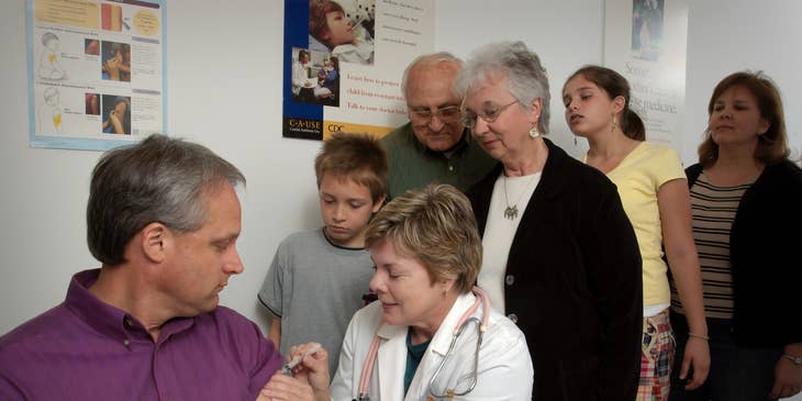 RN Case Manager injects flu vaccine to the patient while promoting wellness to the patient's family members