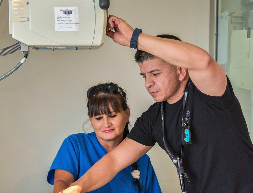 Radiology technician shows how to properly position the hand in an Xray machine to a colleague