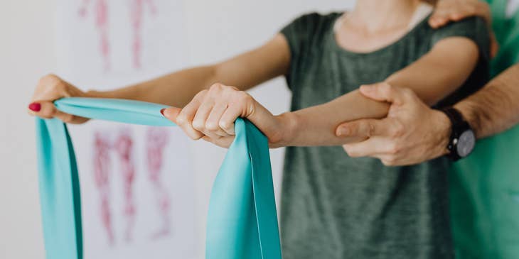 Rehab aide assist a patient is using the elastic band during a therapy session