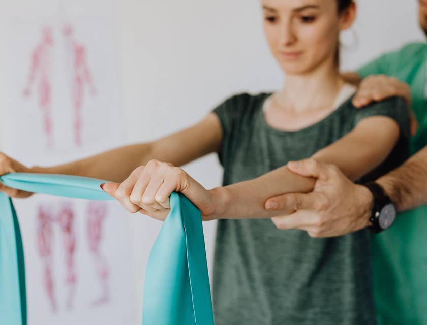 Rehab aide assist a patient is using the elastic band during a therapy session