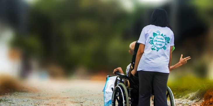 Respite worker accompanies elder patient as she pushes her wheelchair while they stroll outside