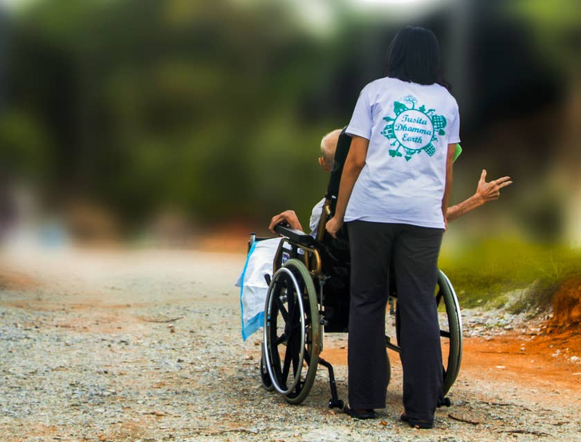 Respite worker accompanies elder patient as she pushes her wheelchair while they stroll outside