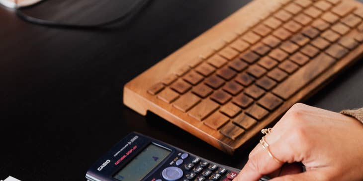 Statistician making computations on sales figures in a calculator to present findings in a report