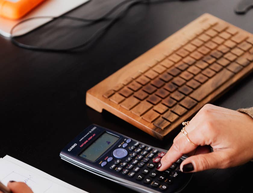 Statistician making computations on sales figures in a calculator to present findings in a report