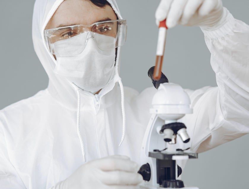 Virologist examines a blood sample under a microscope to check for viruses in a protective suit