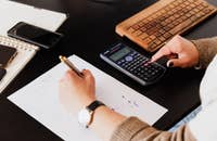 Una contadora utilizando una calculadora y tomando notas en una hoja.