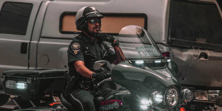 Armed Security Officer reaching for his lapel and riding a motorcycle on his way to report for work