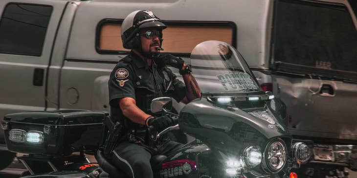 Armed Security Officer reaching for his lapel and riding a motorcycle on his way to report for work