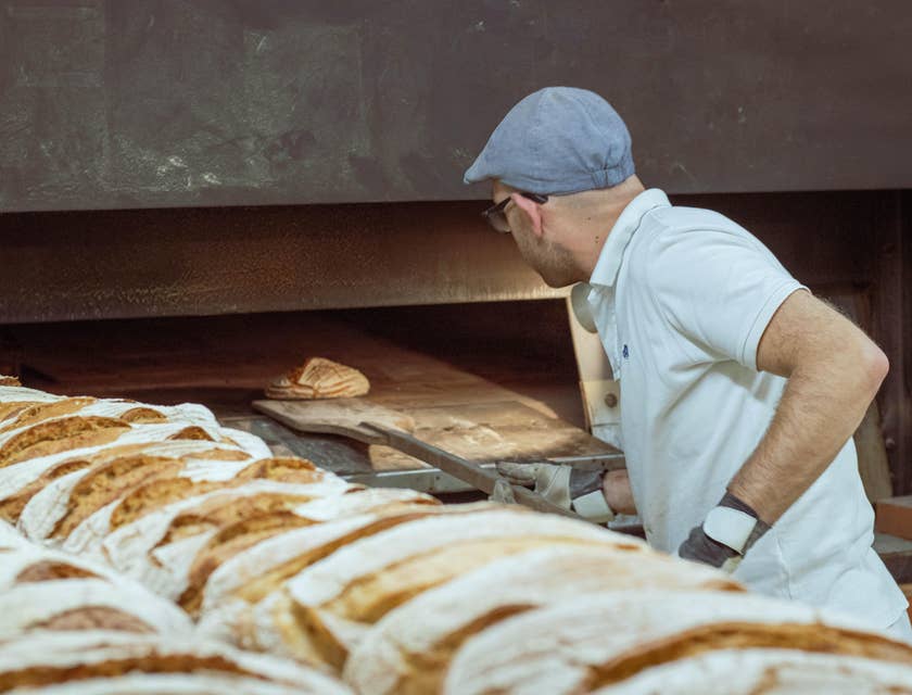Baker taking out a freshly baked bread out of the oven.