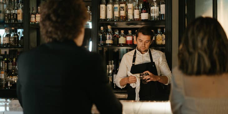 The barback is wiping the glassware after ensuring the the bar is well stocked.