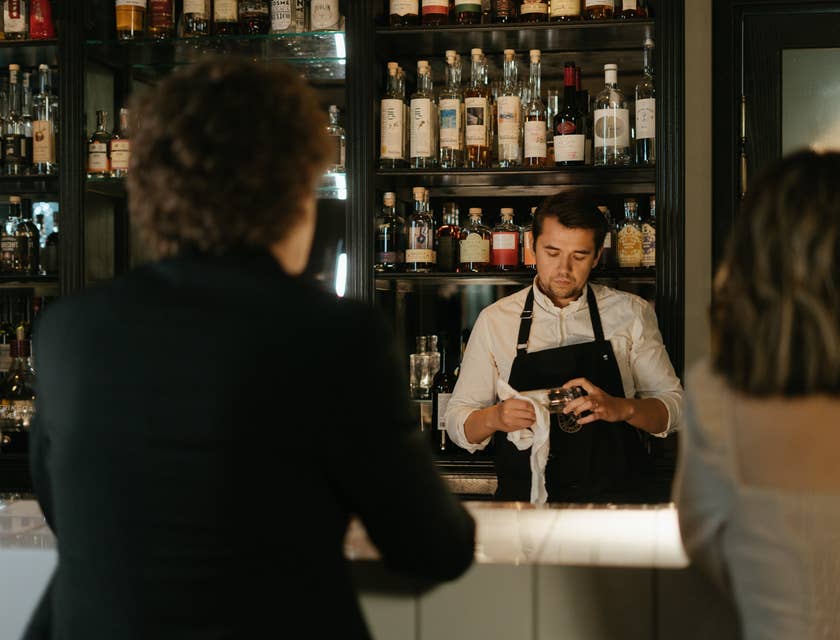 The barback is wiping the glassware after ensuring the the bar is well stocked.