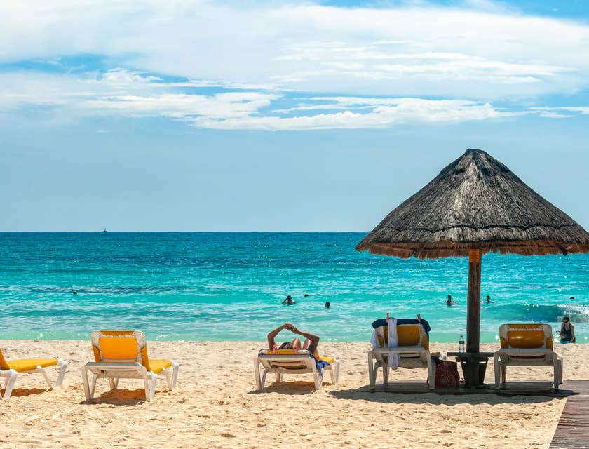 Vista de unos camastros, palapa y el mar de fondo en Cancún.