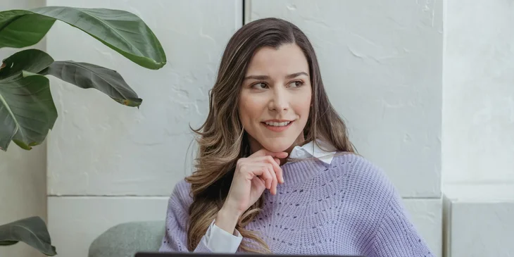 A positive young woman working and sitting in armchair in office.