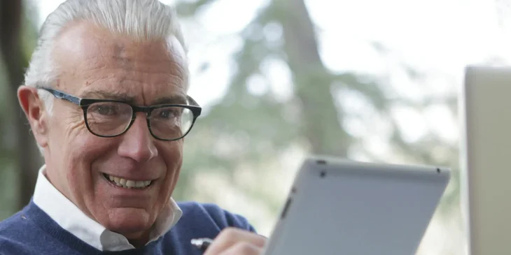 A man in a blue sweater holding a white tablet.