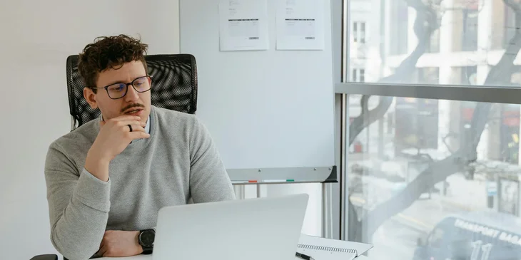 A man in gray sweater wearing eyeglasses while working in the office.