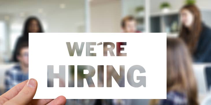 Hand holding a sign saying "We're Hiring"