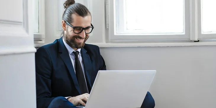 A man in a navy blue suit jacket sitting down using a laptop.