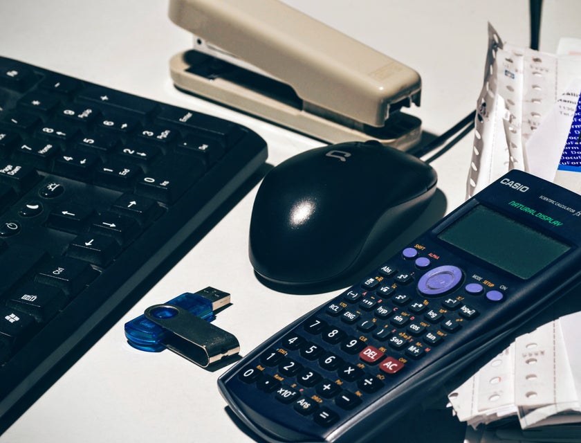 A scientific calculator alongside a keyboard, mouse, stapler, and paperwork.