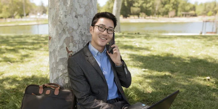 A man sitting on the ground while talking on the phone.