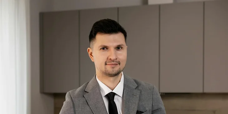 A man in gray suit jacket holding a black folder.
