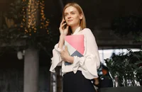 Mulher em uma cafeteria fazendo uma ligação pelo celular.