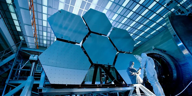 A man in protective gear inspecting the components of a spacecraft.